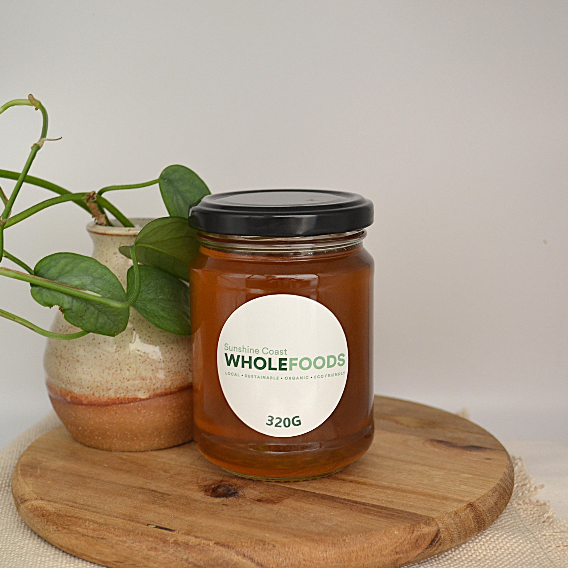 320g Jar of Sunshine coast Wholefoods honey on a wooden board with a plant in the background